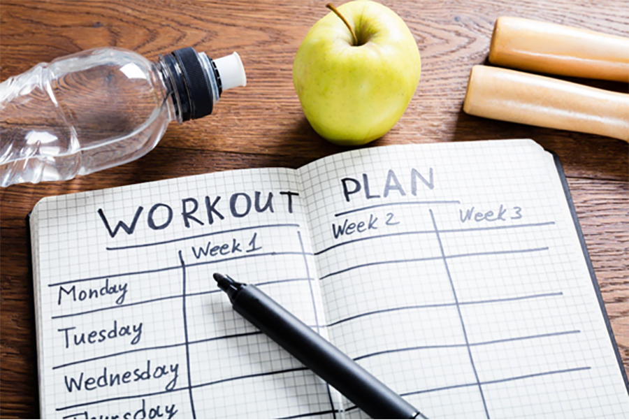 Flat lay of water bottle, apple, jump rope and written workout plan in notebook.